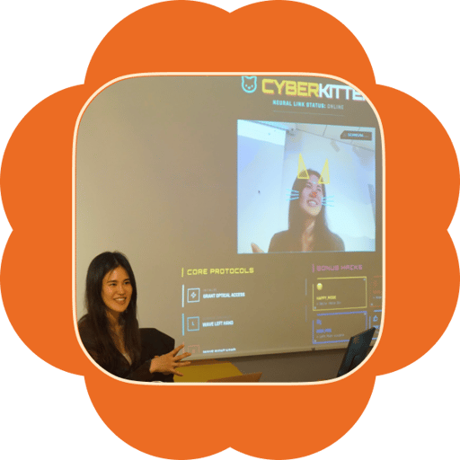A presenter smiling beside a projector screen showing a playful demo app with cat-ear filters